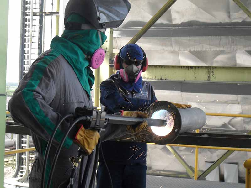 Two workers welding: one is holding a large pipe while the other welds inside of it